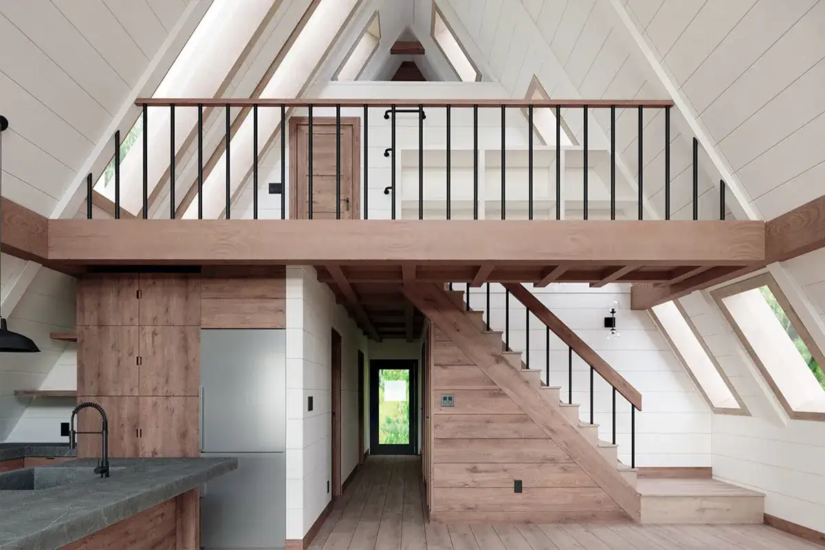 Int&eacute;rieur d'une maison en A avec cuisine, escalier en bois menant &agrave; une mezzanine. Le prix maison en A est abordable pour ce style unique.