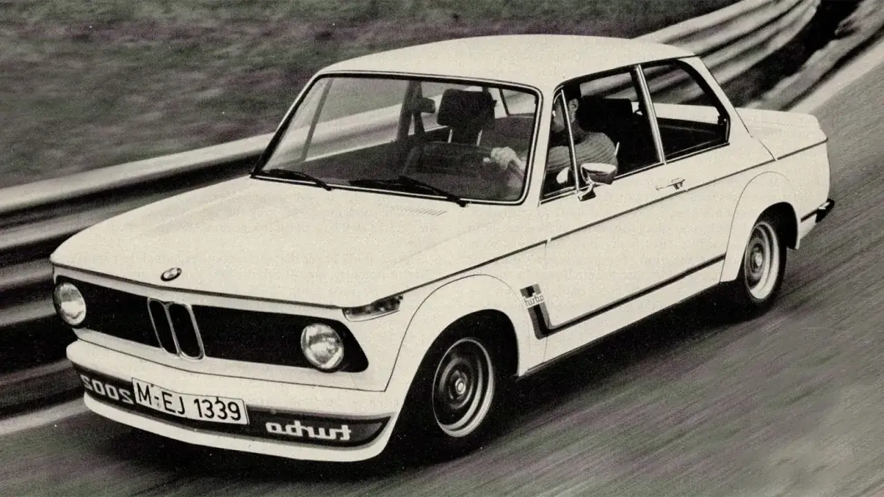 Białe BMW E20 Turbo na torze wyścigowym, z kierowcą za kierownicą.