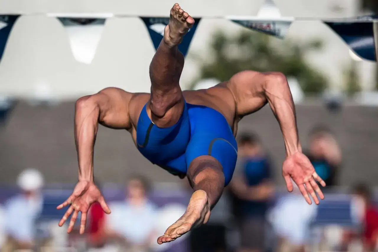A swimmer's powerful swimmer lats are visible as they dive, legs extended and arms reaching forward.