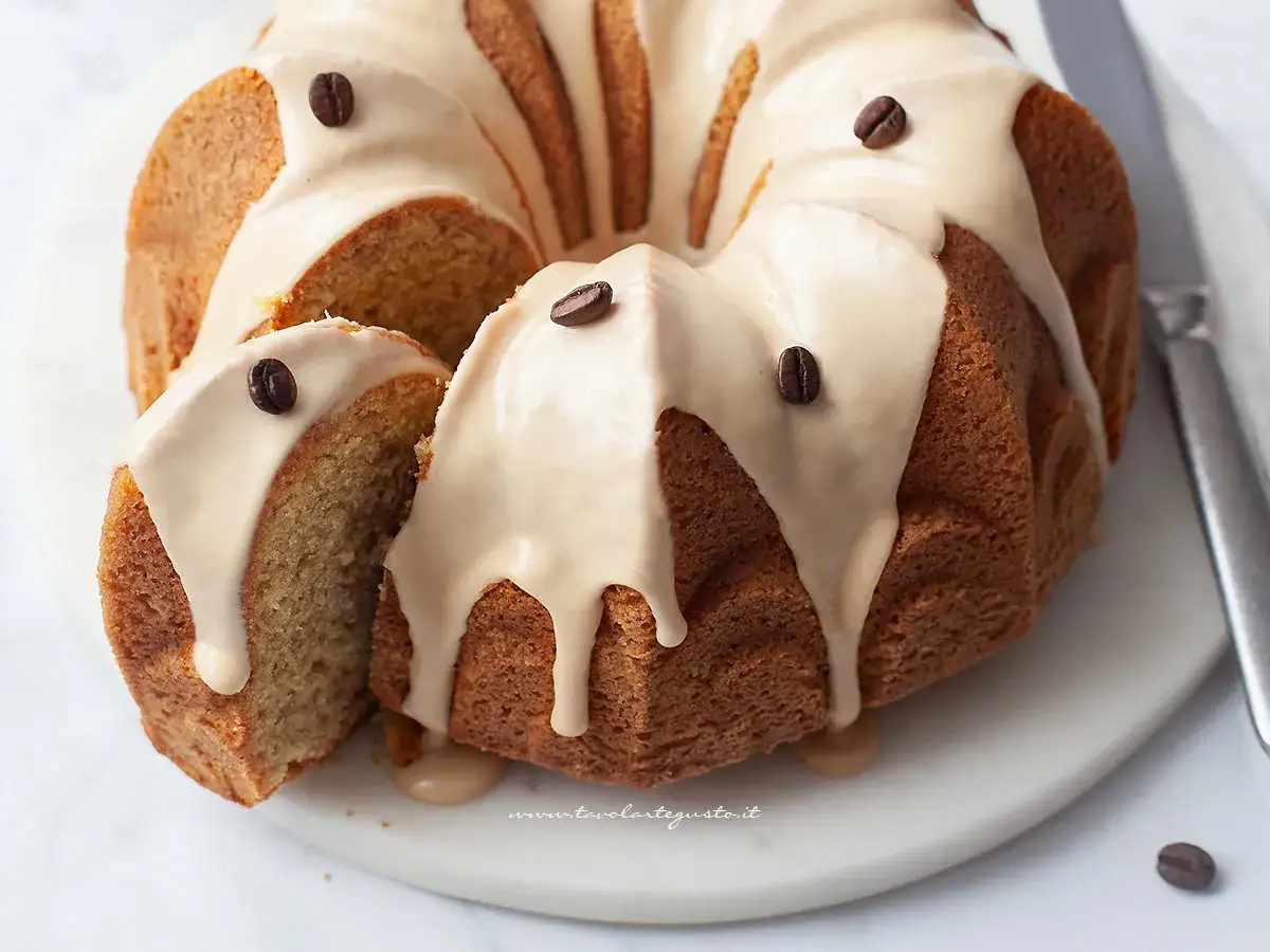 Deliziosa torta al caff&egrave; con glassa chiara e chicchi di caff&egrave; come decorazione. Una fetta &egrave; stata tagliata, rivelando l'interno soffice.