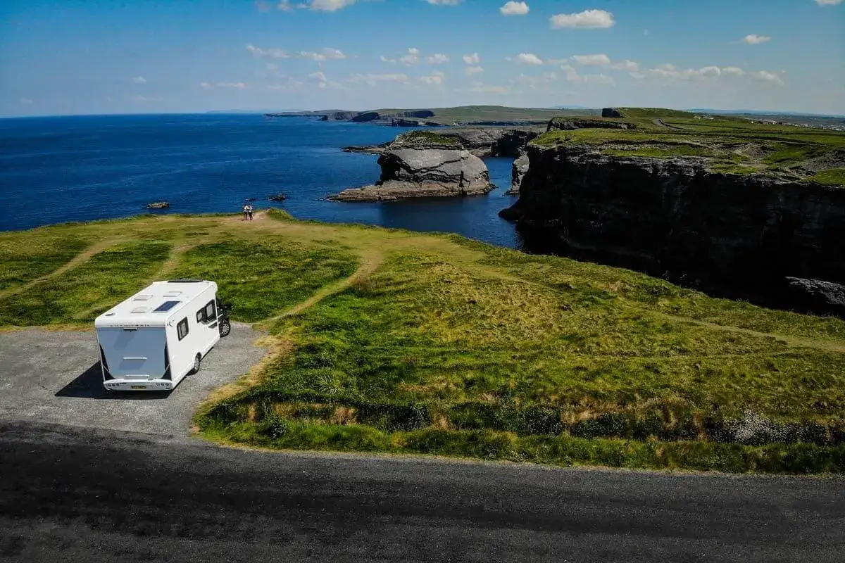 Un camping-car blanc profite d'une vue imprenable sur la c&ocirc;te irlandaise, avec des falaises spectaculaires et l'oc&eacute;an bleu.