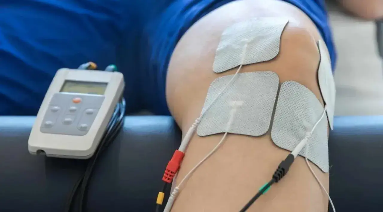 En person får ems behandling på sitt knä. Elektroder är fästa på huden och kopplade till en stimulator.