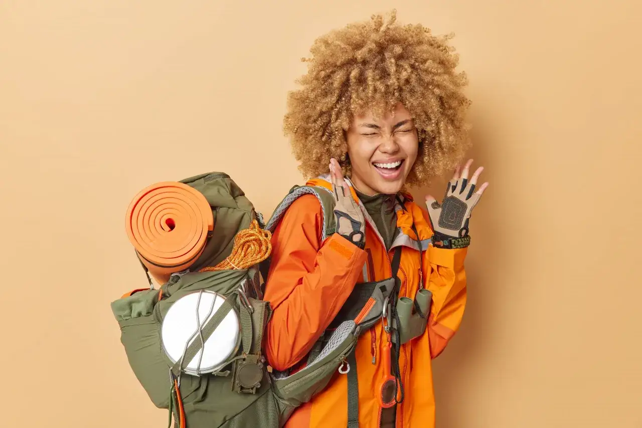 &iexcl;Lista para ir de camping! Con su mochila llena, colchoneta naranja y guantes, esta aventurera sonr&iacute;e emocionada.