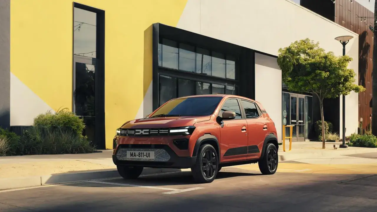 Pomarańczowy, elektryczny Dacia Spring, który może być odpowiedzią na pytanie, ile kosztuje najtańszy samochód elektryczny, zaparkowany przed nowoczesnym budynkiem.