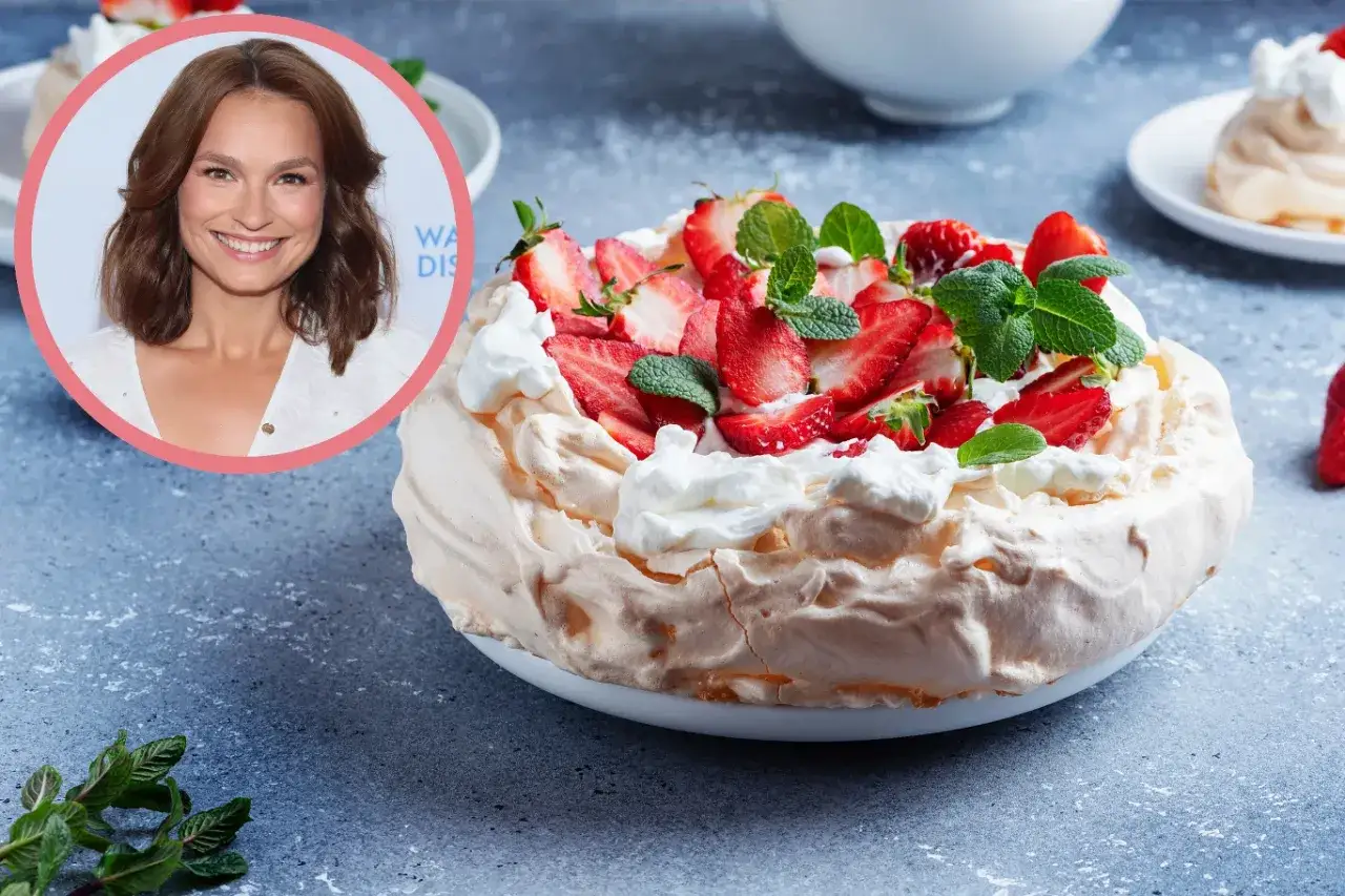 Uśmiechnięta kobieta obok pysznego tortu pavlova ze świeżymi truskawkami i bitą śmietaną.