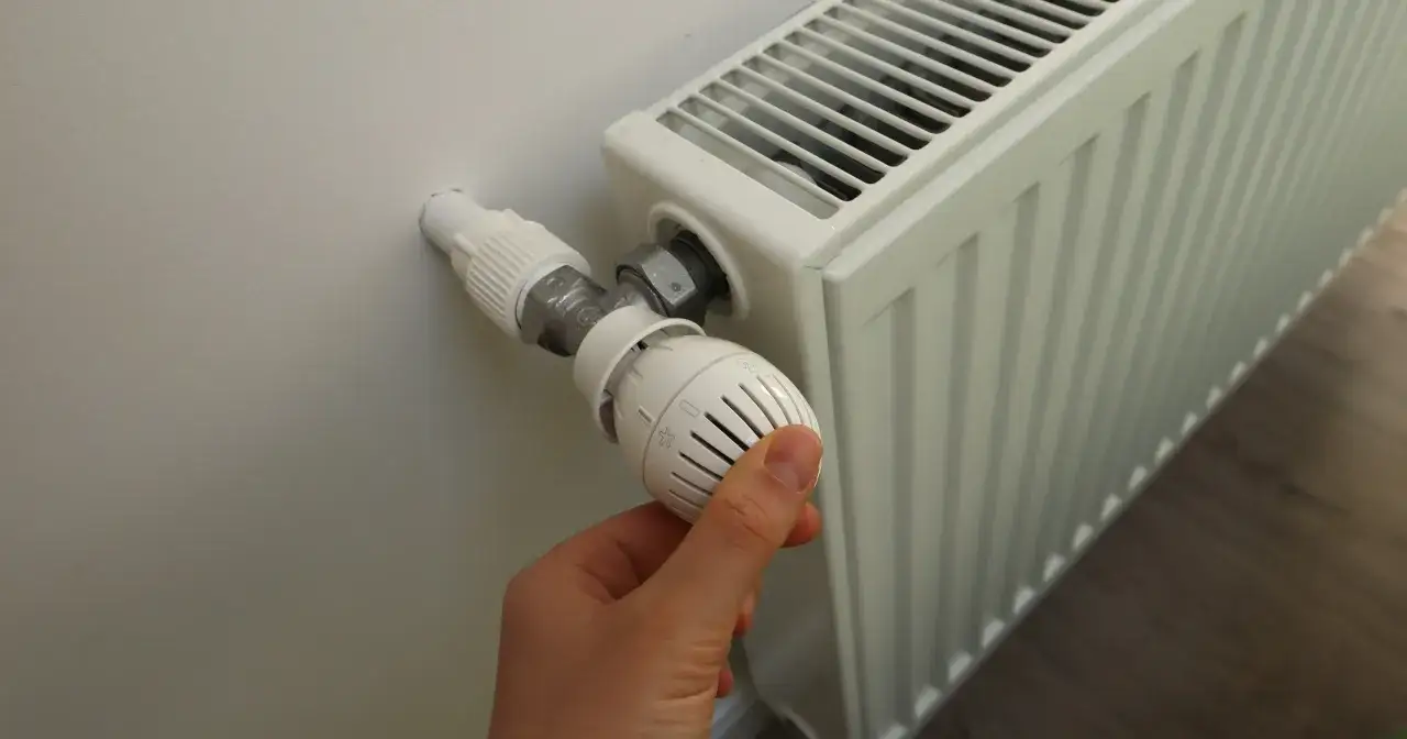 Dłoń kręci termostatem grzejnika, przygotowując dom na zimę, kiedy zaczyna się sezon grzewczy.