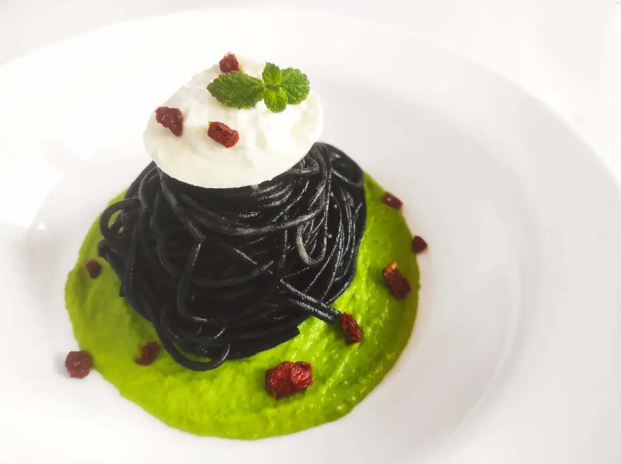 Spaghetti al nero di seppia, serviti su crema di piselli, con una quenelle di ricotta e menta.