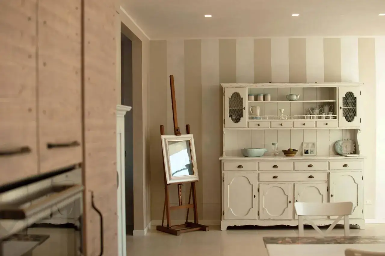 Un mobile da cucina bianco, con un'aria vissuta, incarna lo stile shabby chic arredamento. Un cavalletto con specchio completa la scena.