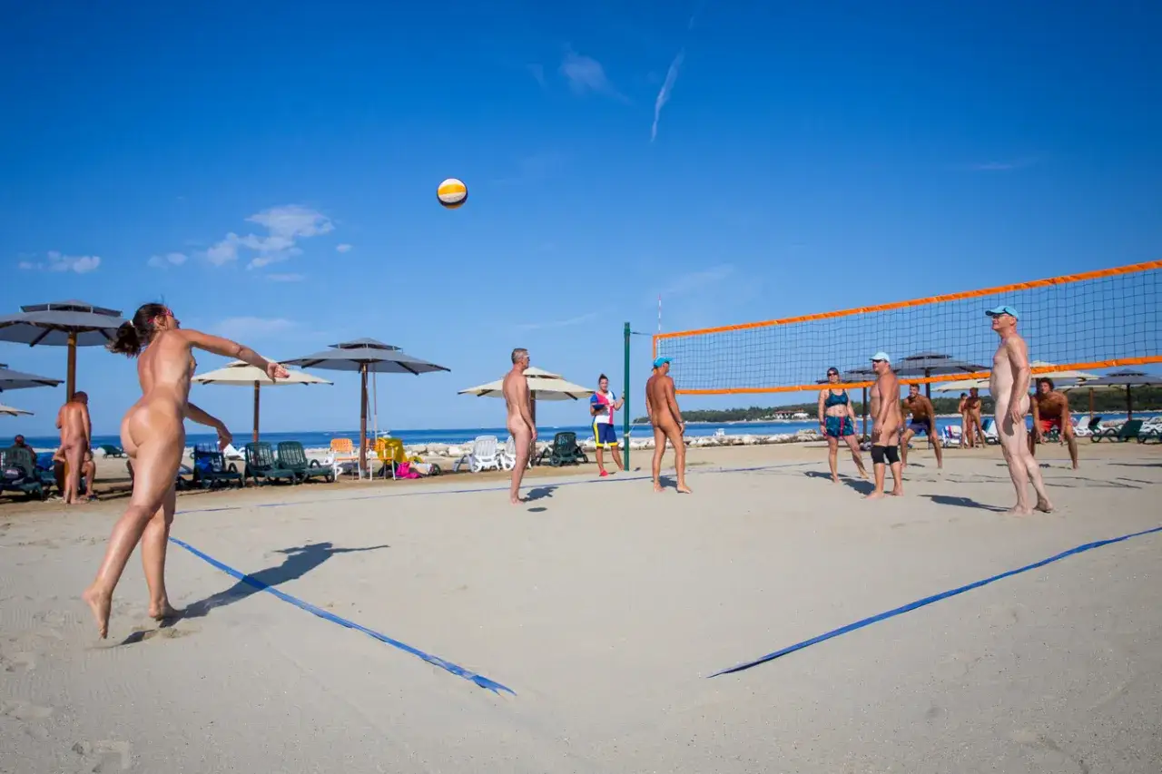 Nudystyczna plaża w Valalta naturist camp. Ludzie grają w siatkówkę plażową pod błękitnym niebem.