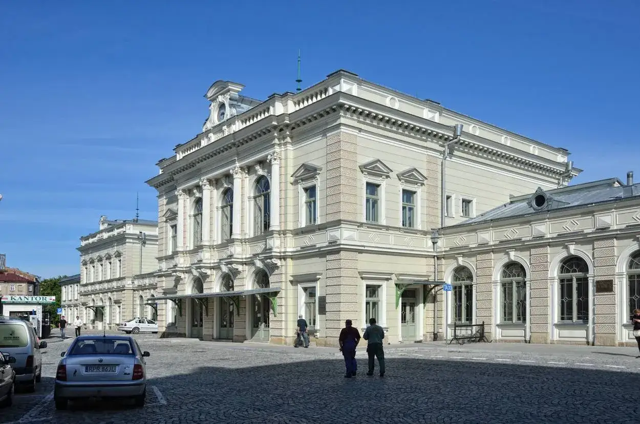 Elegancki budynek dworca kolejowego w Przemyślu, z charakterystyczną architekturą i brukowanym placem przed nim.