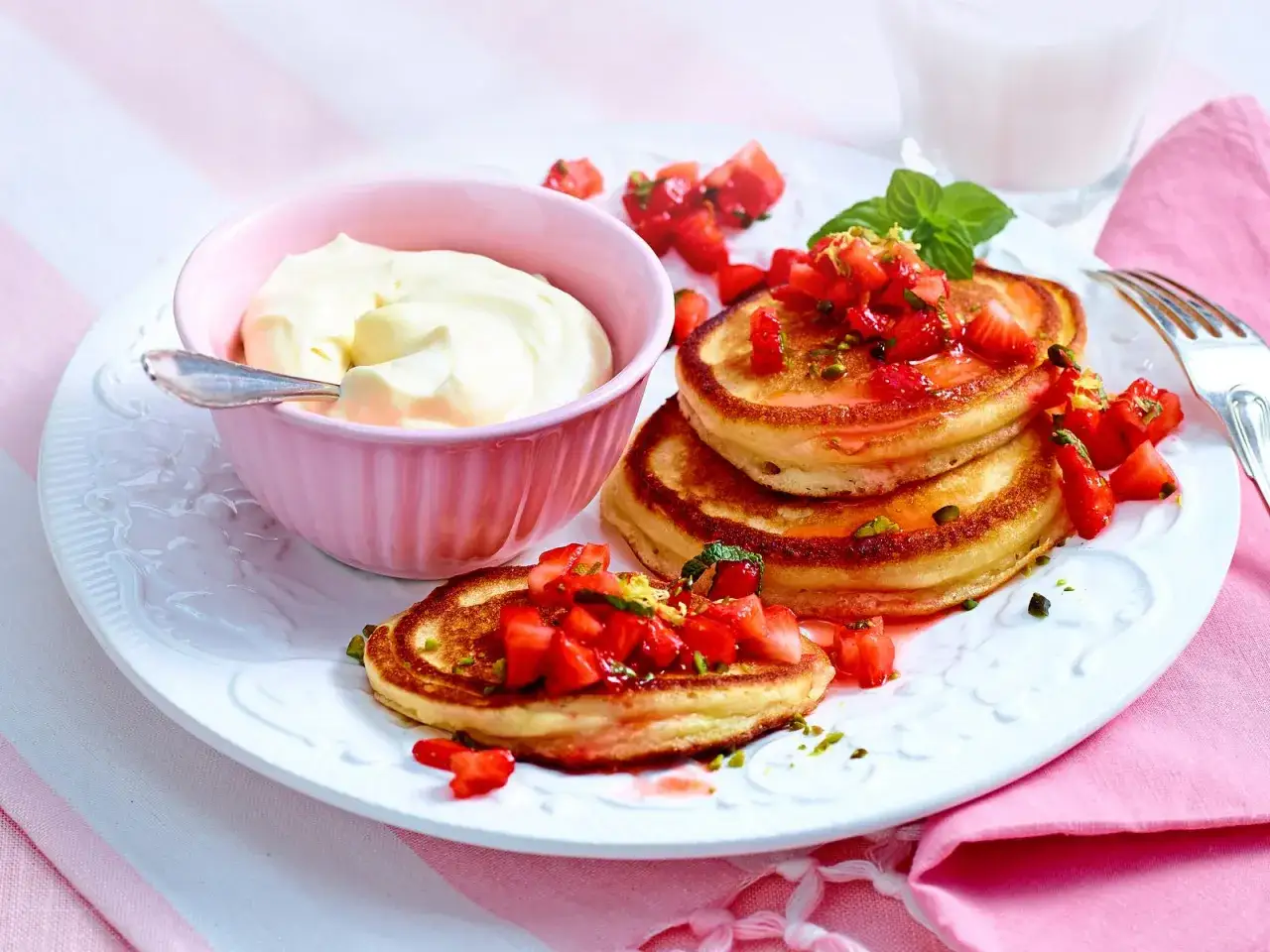 Erdbeer Pancakes mit frischen Erdbeeren, Sahne und gehackten Pistazien auf einem Teller. Ein köstliches Frühstück!