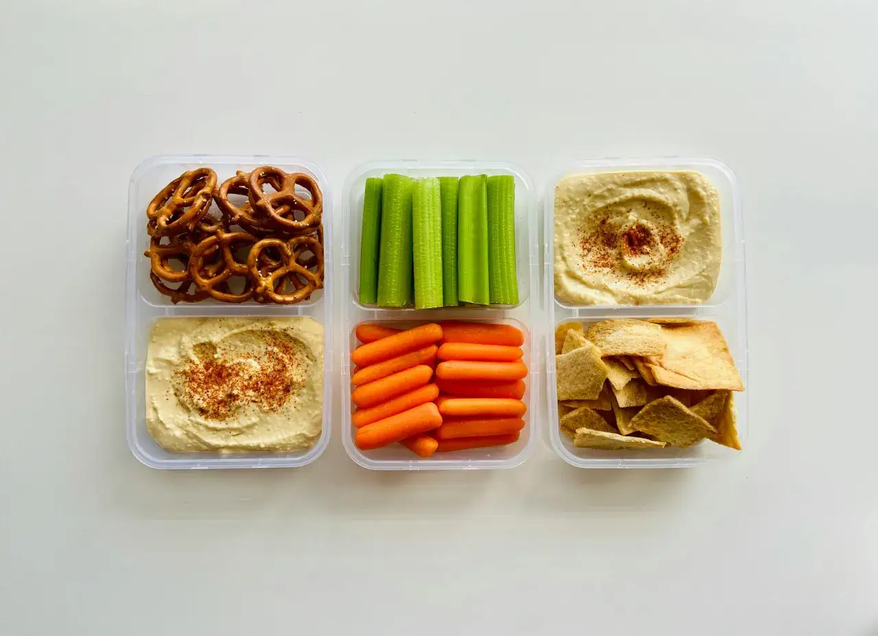 Contenedores con pretzels, bastones de apio, zanahorias baby, hummus y trozos de pan pita. Ideales para meriendas saludables para bajar de peso.