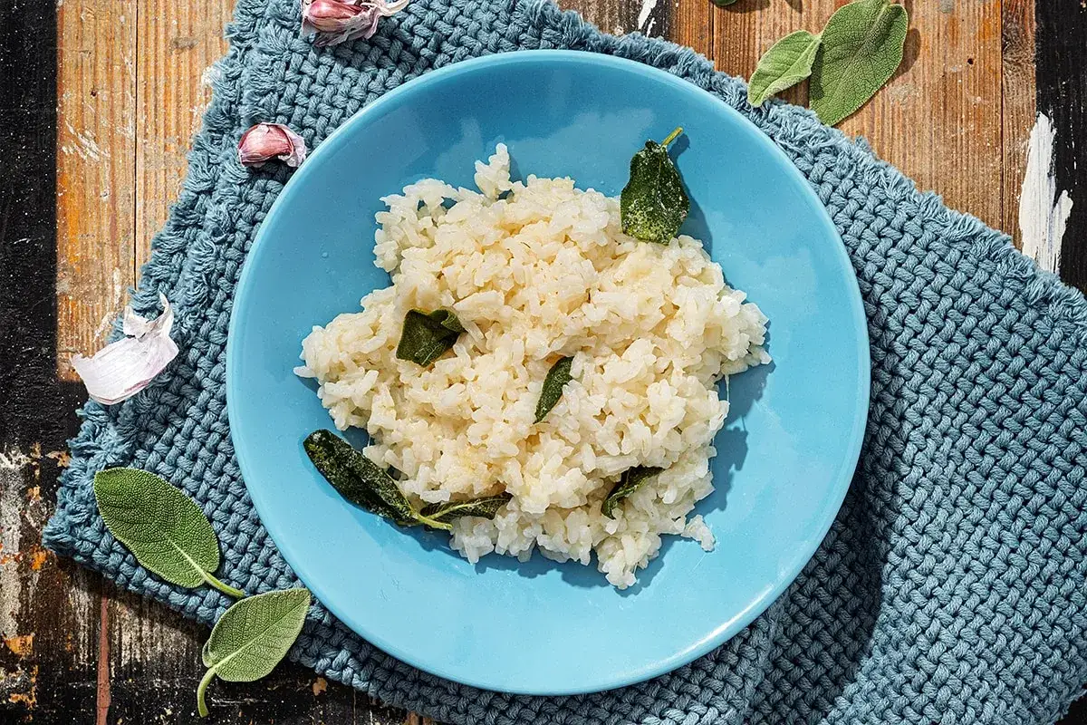 Piatto di riso in cagnone, profumato con salvia e aglio, servito su un tovagliolo blu intrecciato.