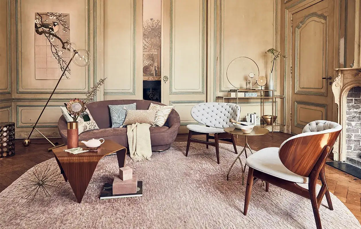 Een sfeervol interieur klassiek met een paarse bank, witte fauteuils en een houten bijzettafel. Een vloerlamp met glazen bol verlicht de ruimte.