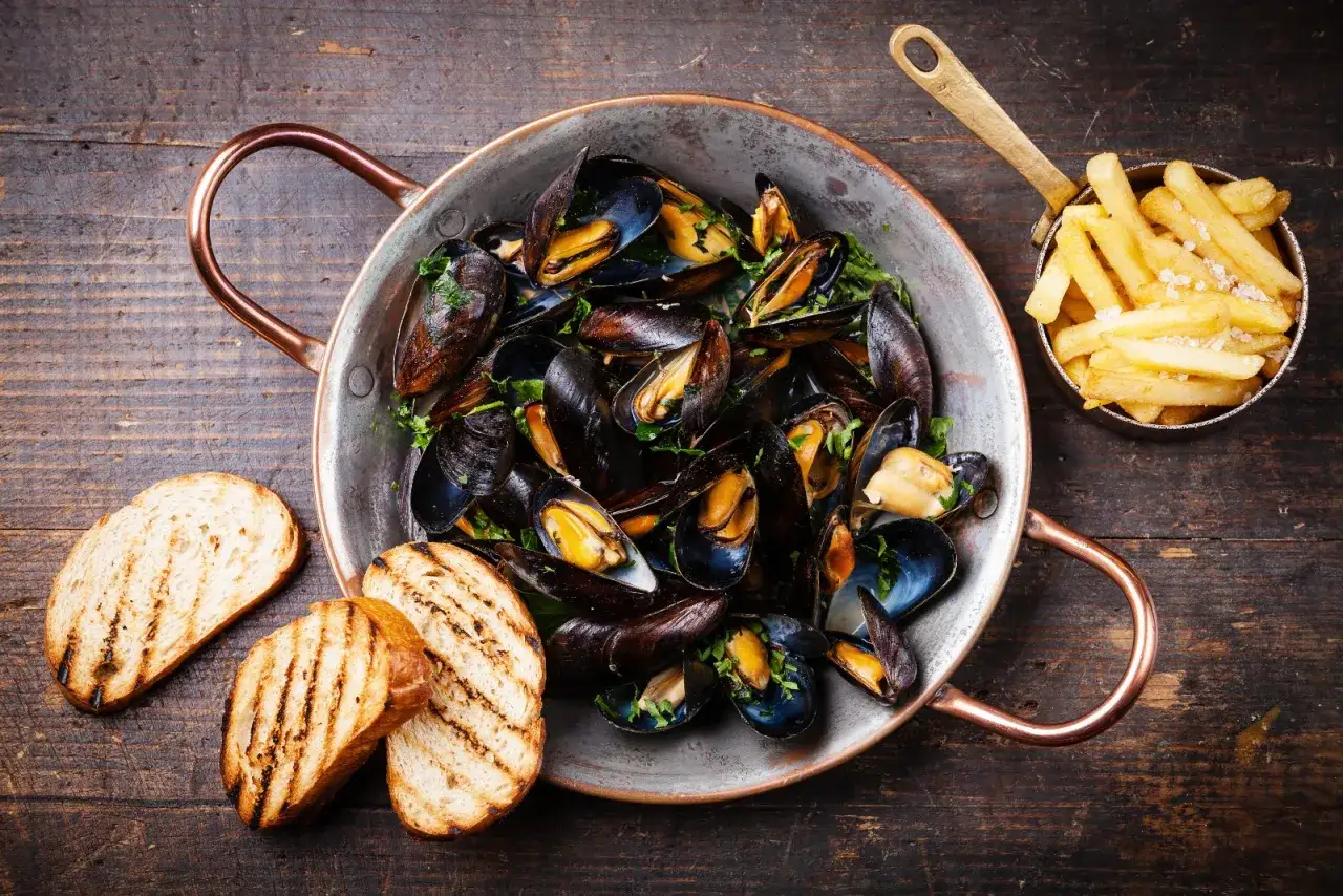 Moules marinières et frites, un plat typique normandie, servi dans une poêle en cuivre avec du pain grillé.