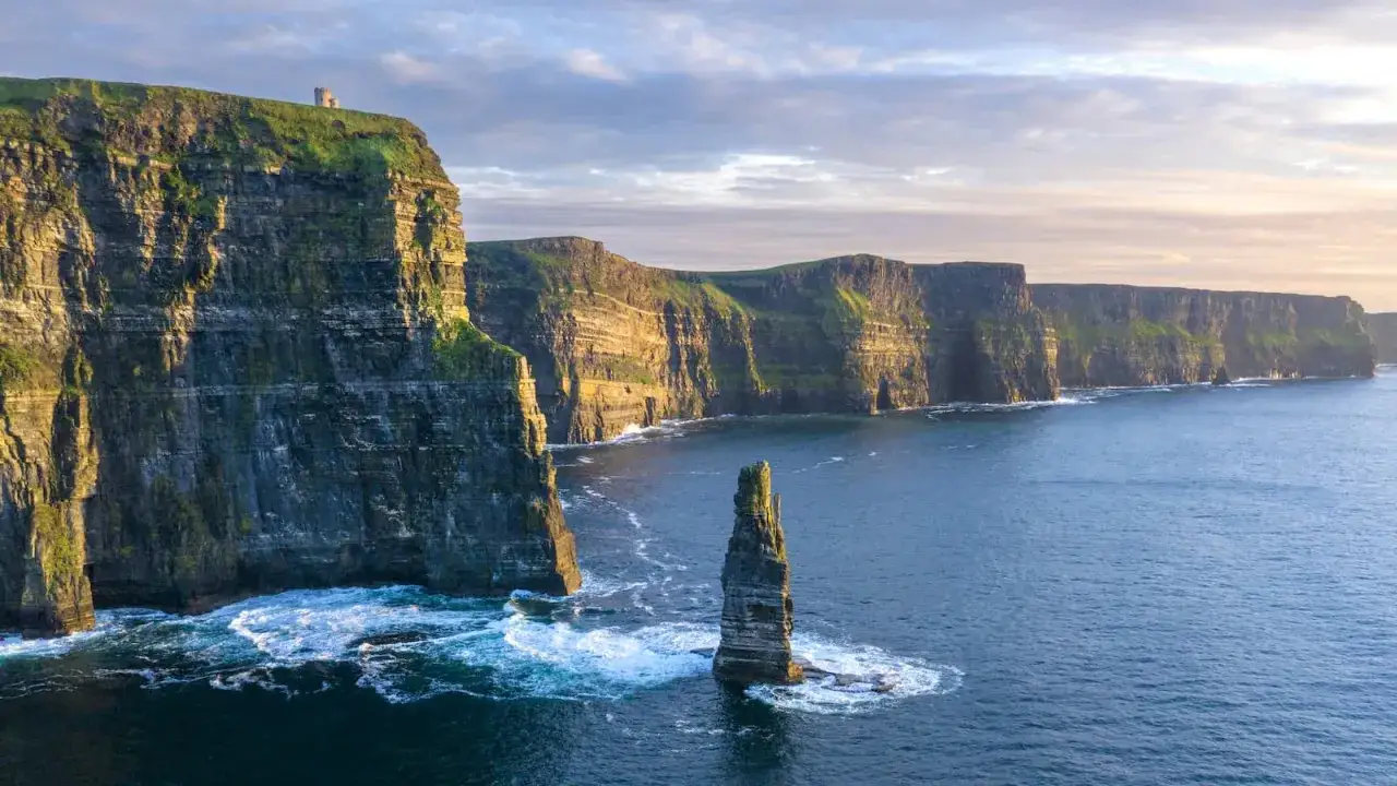 Majestatyczne klify Irlandii wcinają się w błękitny ocean. Na szczycie jednego z nich stoi samotna wieża.