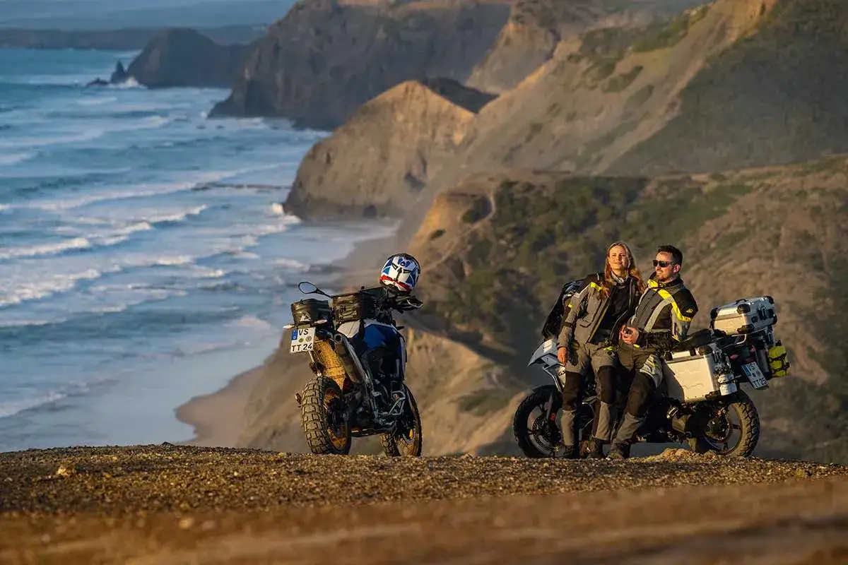 Para motocyklistów odpoczywa na klifie, podziwiając dzikie wybrzeże Algarve. Ich motocykle gotowe do dalszej podróży.