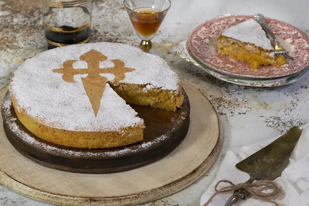 Tarta de Santiago, espolvoreada con az&uacute;car glas y decorada con la Cruz de Santiago. Una porci&oacute;n ya servida en un plato.