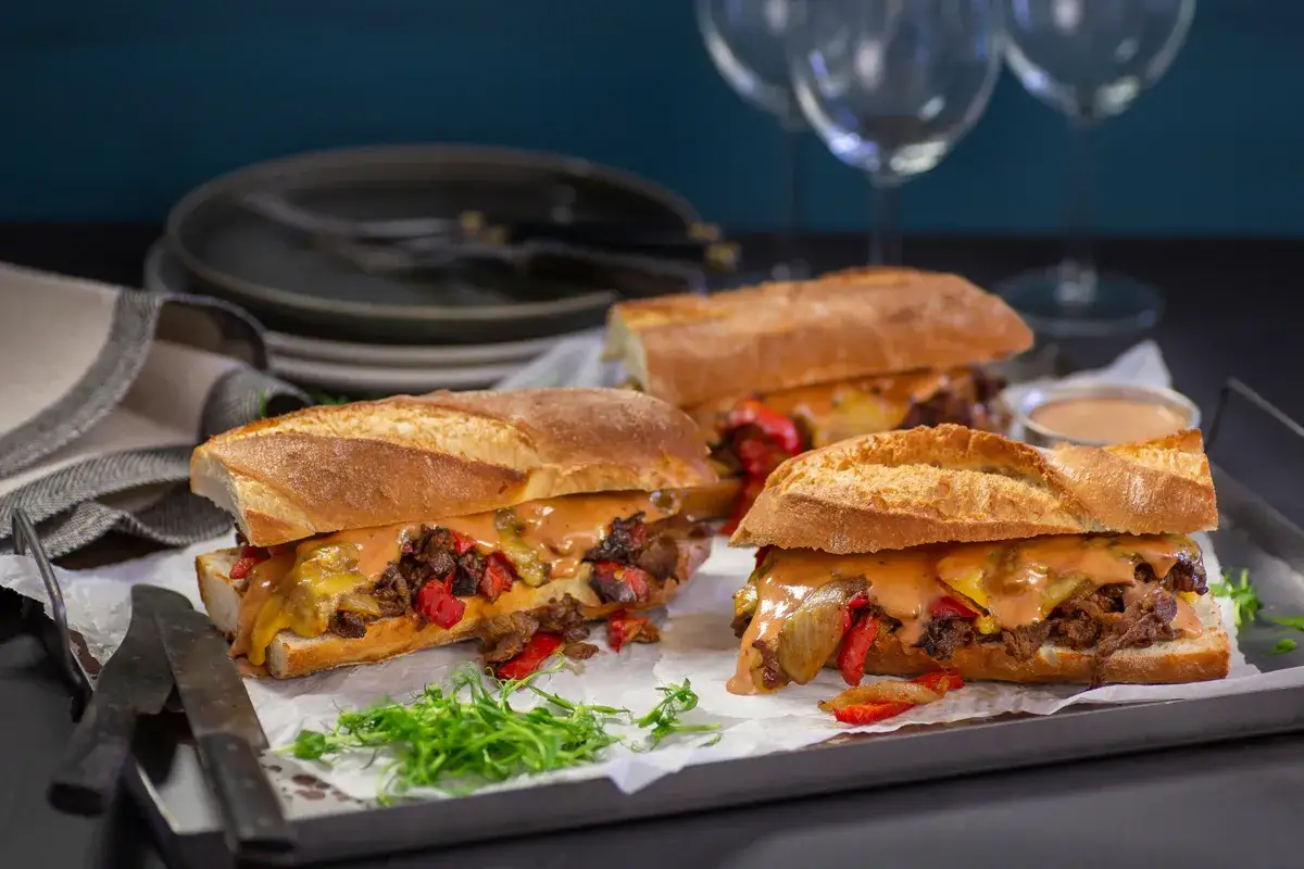 Tre saftiga steak sandwich med sm&auml;lt ost och gr&ouml;nsaker p&aring; en bricka, redo att avnjutas.