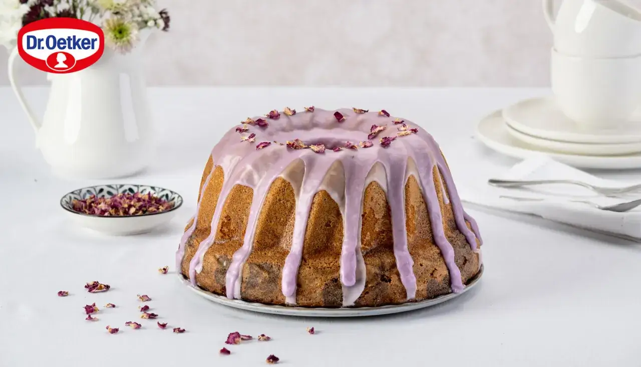 Ein köstlicher Marmorkuchen mit Kirschen, verziert mit zarter lila Glasur und Rosenblättern.