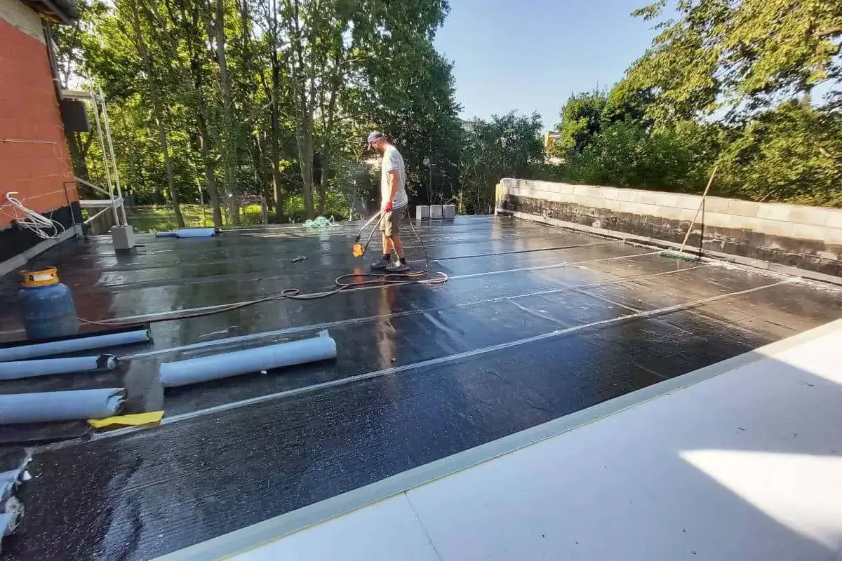 Pracownik wykonuje hydroizolację tarasu na dachu, używając palnika do zgrzewania papy.