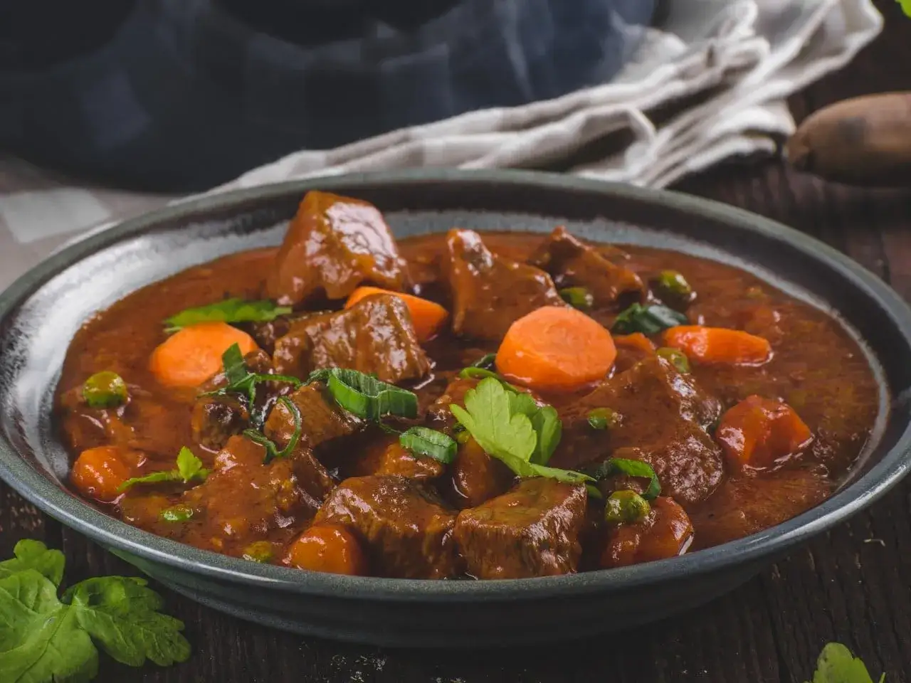 Un reconfortante plato de menestra de ternera con trozos de carne tierna, zanahorias y guisantes en una rica salsa.