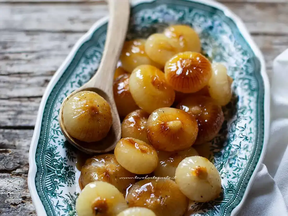 Cipolline in agrodolce in padella con aceto balsamico, lucide e caramellate, servite su un piatto decorato.