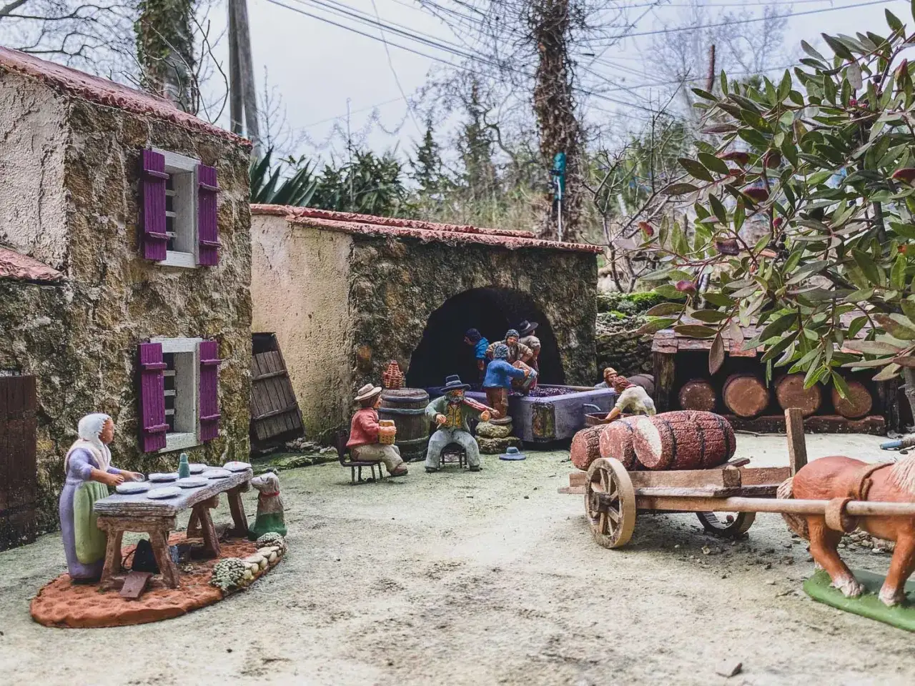 Maquette de cr&egrave;che de No&euml;l : sc&egrave;ne de village avec personnages, maisons en pierre, tonneaux et charrette tir&eacute;e par un cheval.