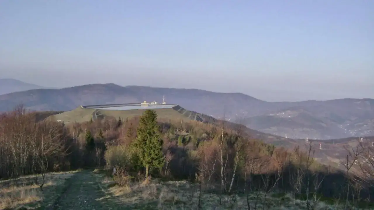 Zbiornik na szczycie g&oacute;ry Żar, otoczony lasem i g&oacute;rami w tle.
