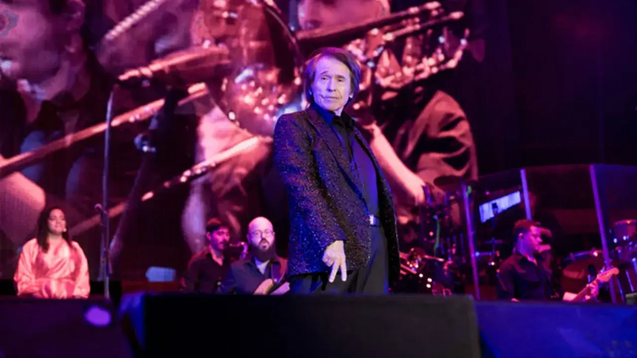 Raphael, con su chaqueta brillante, cautiva en uno de sus conciertos. A su lado, m&uacute;sicos y coristas completan la escena.