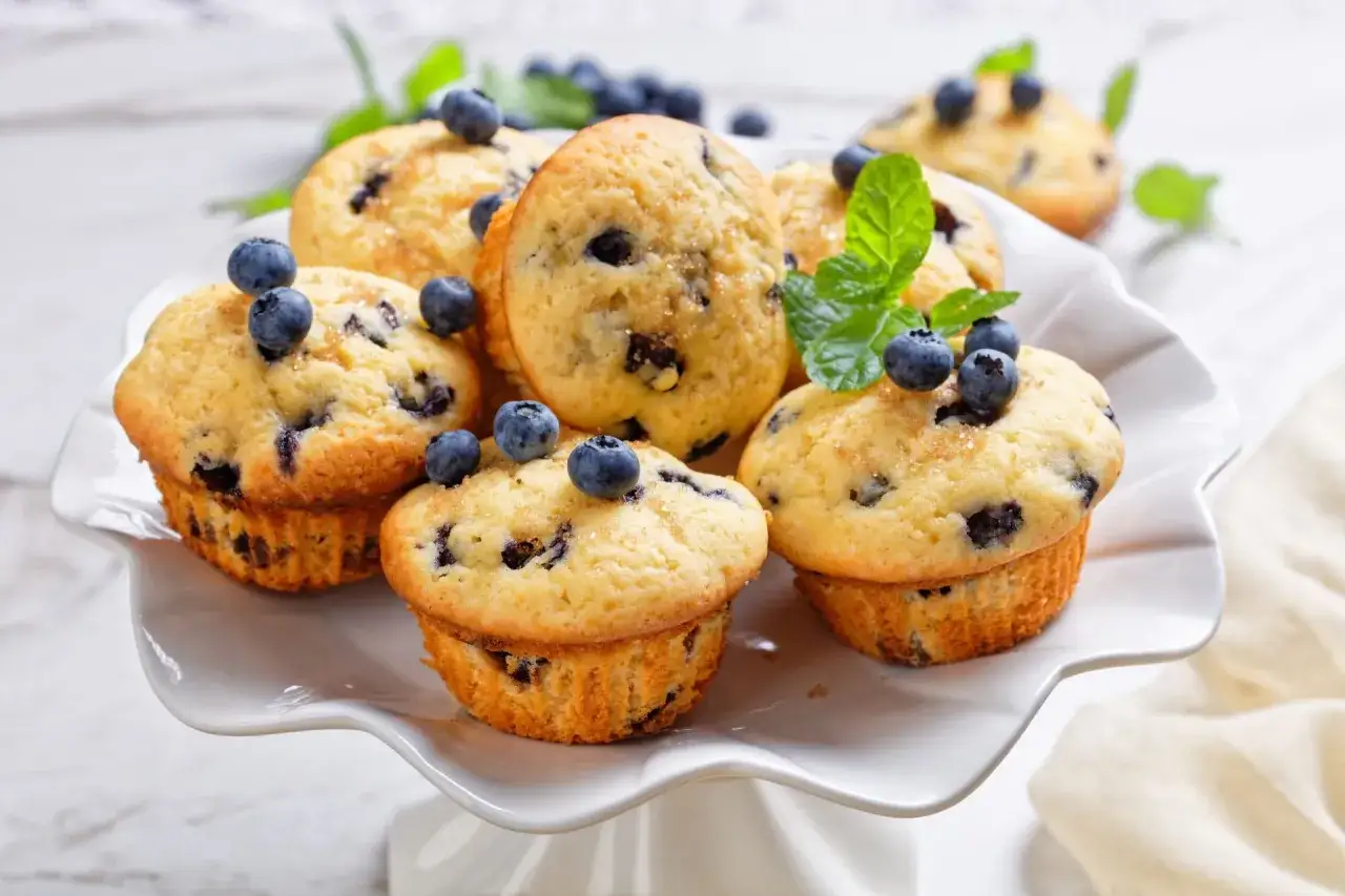 Pyszne keto muffiny z mąki migdałowej, udekorowane świeżymi borówkami i listkami mięty, kuszą apetycznym wyglądem.