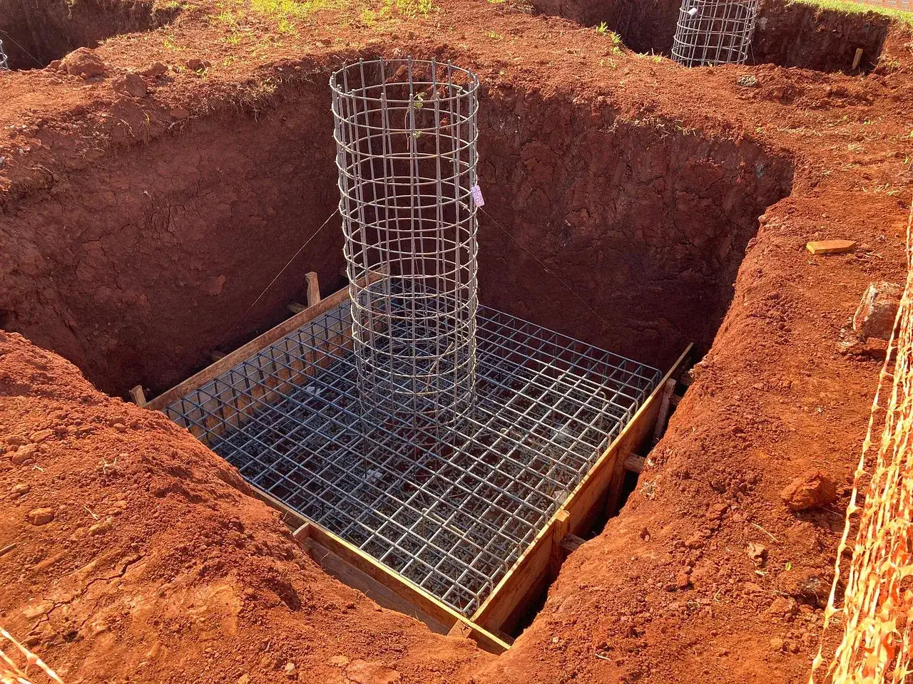 Gotowe zbrojenie słupa fundamentowego w wykopie. Metalowa siatka i pionowe pręty czekają na beton.