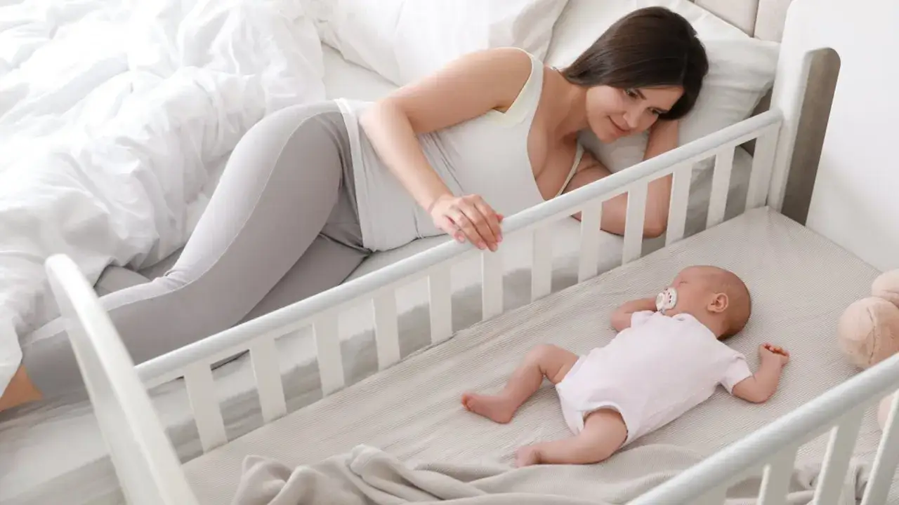Madre observa tiernamente cómo duermen los bebes en su cuna. El bebé, con un chupete, descansa plácidamente.