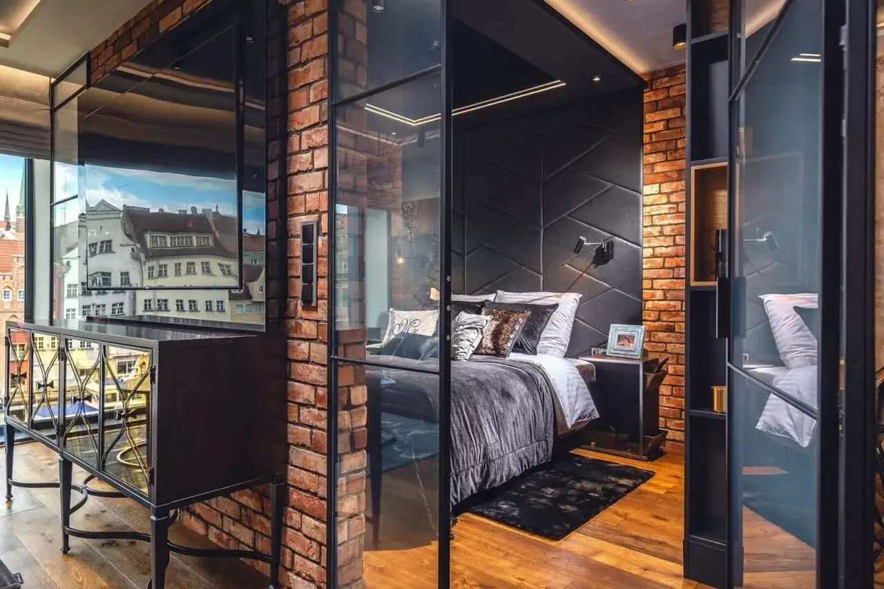 Nowoczesny green loft z cegłą i szkłem. Sypialnia z wygodnym łóżkiem i widokiem na miasto.