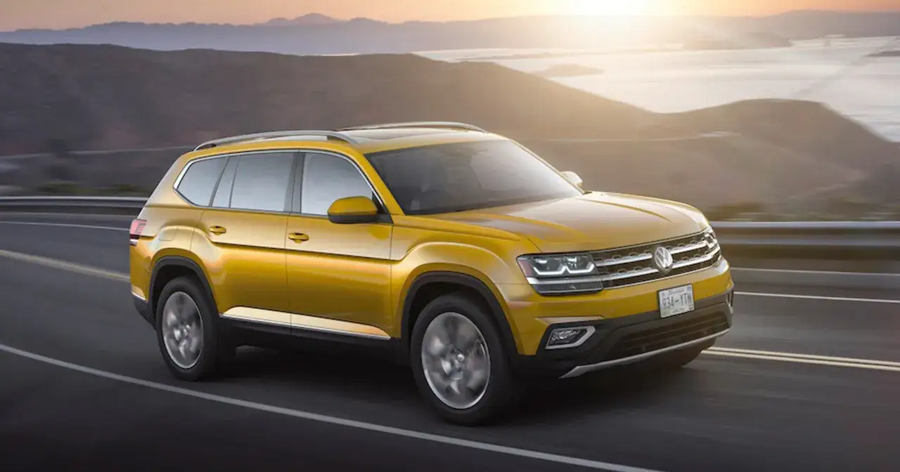 Żółty VW Atlas jedzie po drodze w górach o zachodzie słońca.