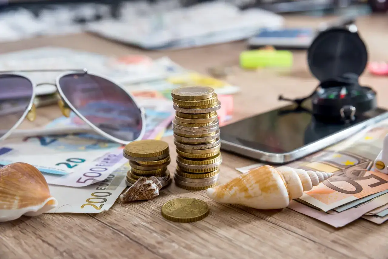 Euro banknoty, monety, okulary przeciwsłoneczne, muszle i kompas na telefonie – wszystko gotowe na podróż z usługą wielowalutową mBank.