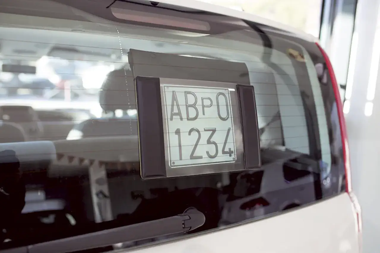 Targa prova ABPO 1234 fissata al lunotto posteriore di un'auto bianca.