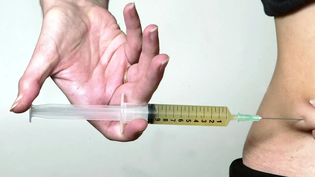Eine Hand hält eine Spritze mit gelblicher Flüssigkeit, bereit für Clexane Spritzen in den Bauch.