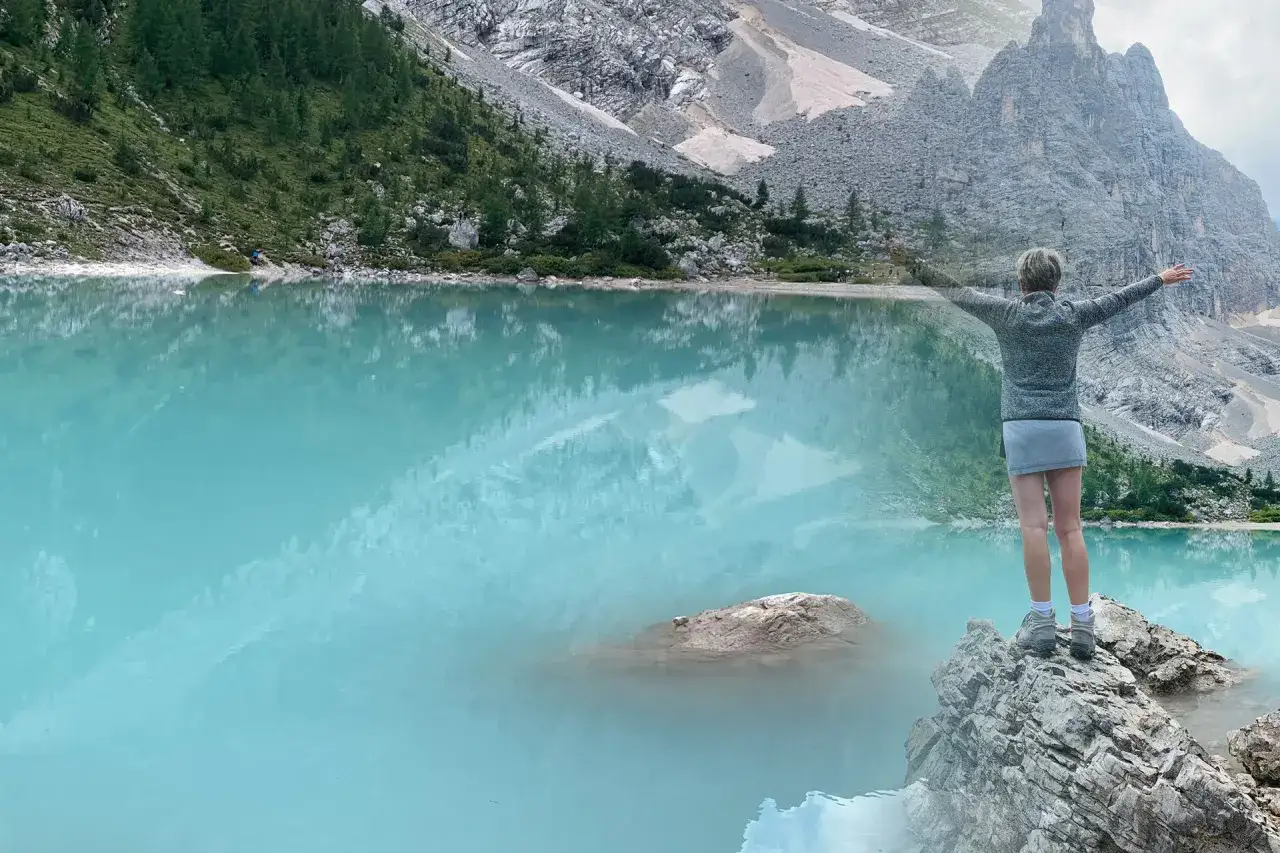 Donna con braccia aperte ammira il lago di Sorapis. Scopri come arrivare a questo gioiello delle Dolomiti.