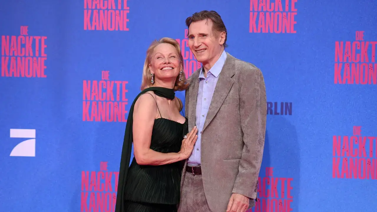 Liam Neeson e Pamela Anderson sorridono sul red carpet, con lo sfondo di 