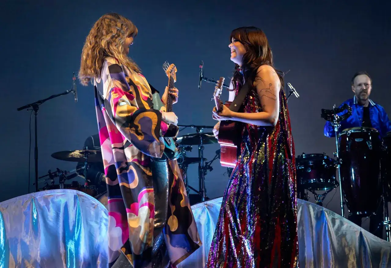 Tv&aring; musiker p&aring; scen, en med bas och en med gitarr, glatt leende. En trummis i bakgrunden. En first aid kit konsert kan beh&ouml;vas om publiken blir f&ouml;r exalterad.