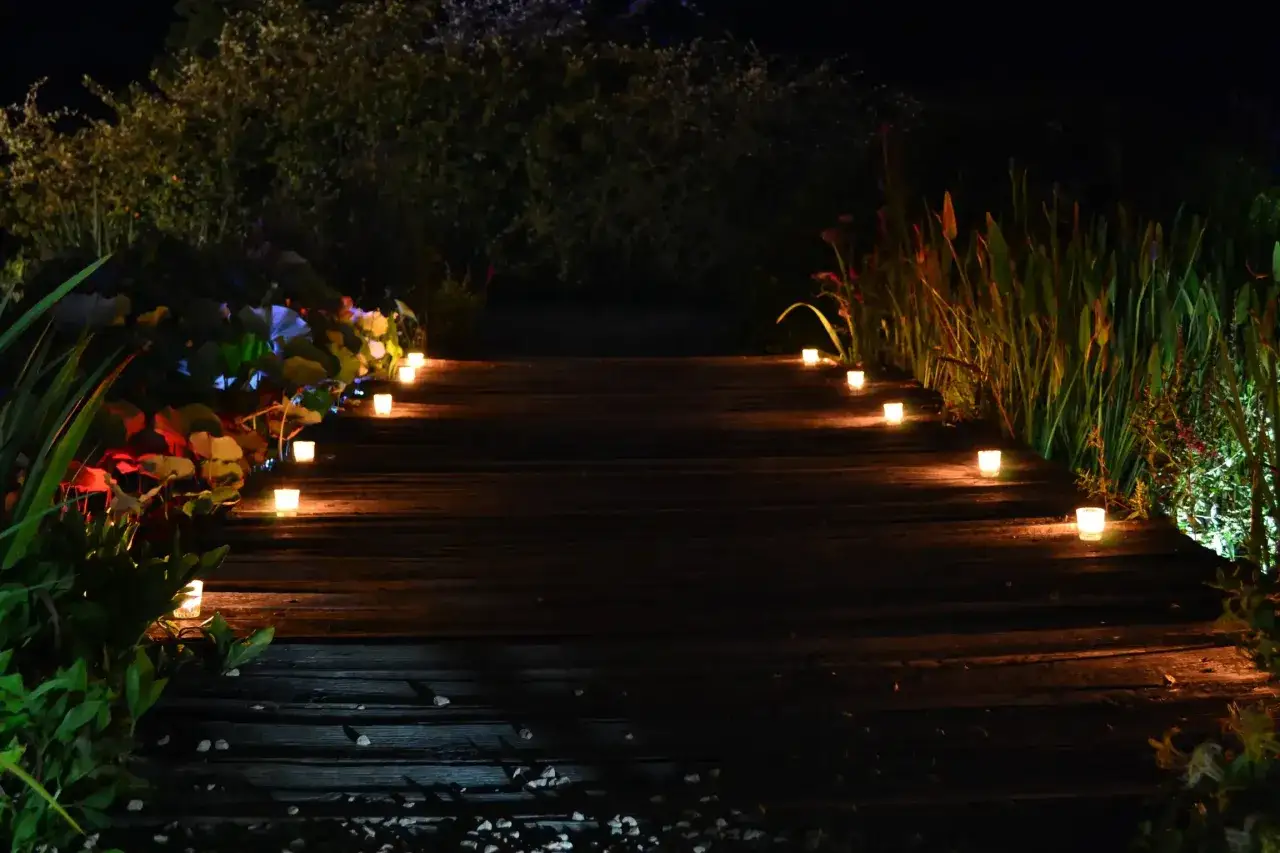 Romantische gartenbeleuchtung ideen: Ein Holzweg wird von kleinen Kerzen beleuchtet, die eine warme, einladende Atmosphäre schaffen.