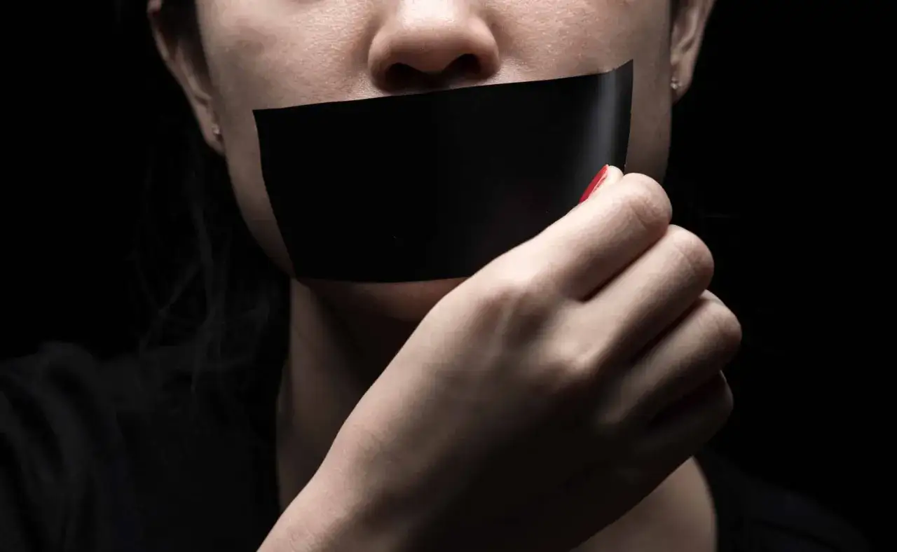 Une bouche bâillonnée par du ruban adhésif noir, une main tentant de le retirer. L'effet du silence sur le manipulateur est palpable.