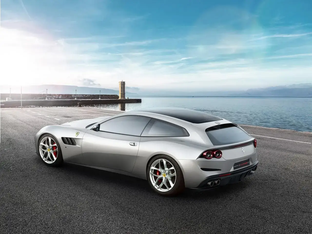 Srebrne Ferrari GTC4Lusso zaparkowane nad morzem, z latarnią morską w tle.