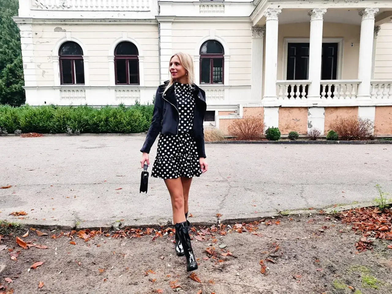 Kobieta w grochy i błyszczące kalosze stylizacje. Elegancka sukienka i ramoneska tworzą modny zestaw.