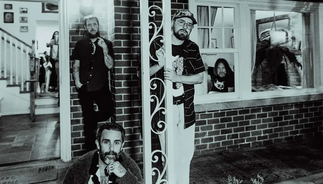 Band of Horses poserar utanför ett hus i Stockholm. En medlem tittar ut genom ett fönster.