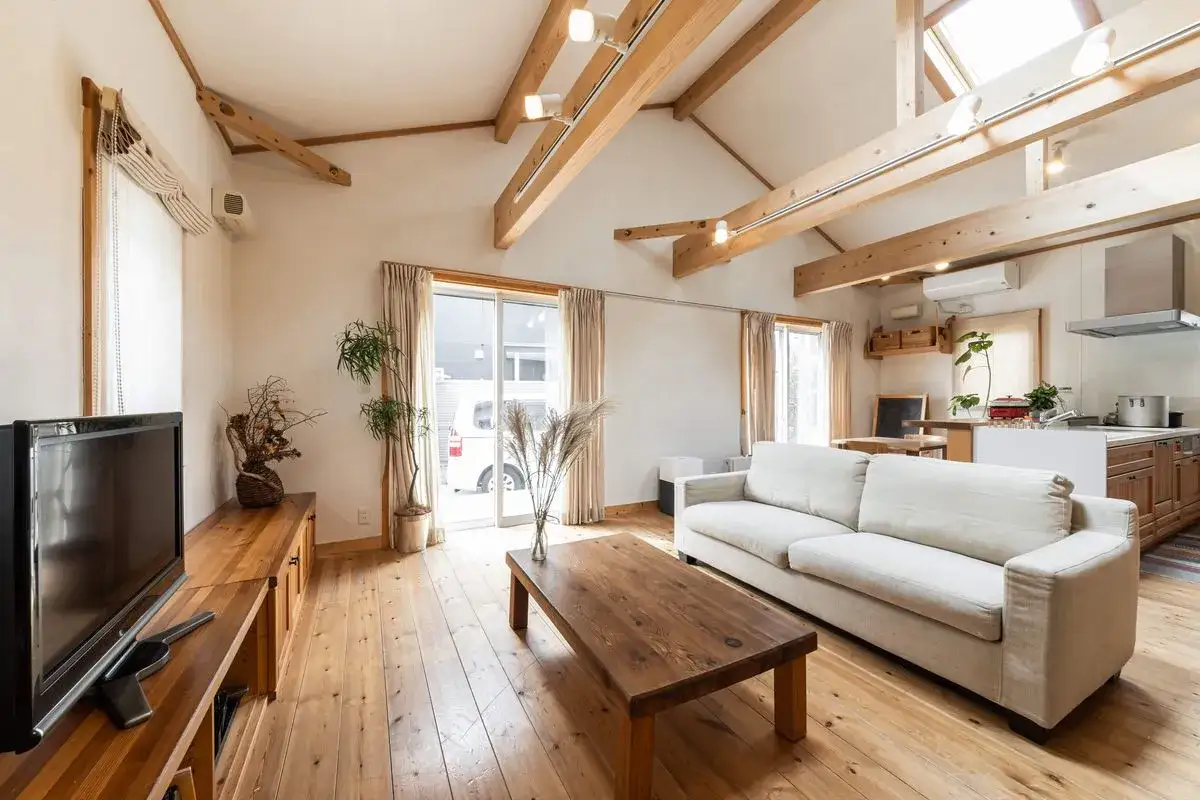 Jasny, przestronny salon z widocznym drewnianym sufitem, belkami i oknami dachowymi. Wygodna sofa i drewniany stolik kawowy tworzą przytulną atmosferę.
