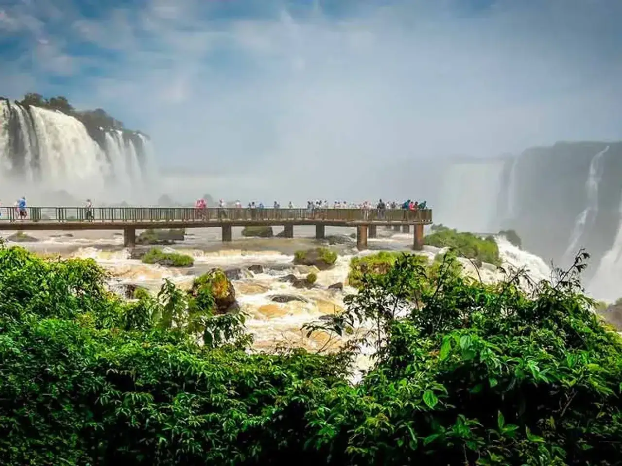 Pasarela sobre el r&iacute;o Iguaz&uacute;, con visitantes admirando las imponentes cataratas del Iguaz&uacute;.