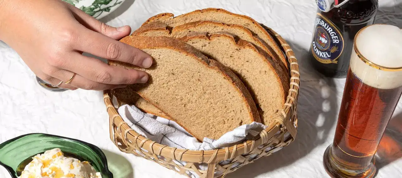 Ein Korb mit Scheiben von rustikalem Brot, daneben ein Glas Bier und eine Flasche. Perfekt für eine deftige Brotzeit.