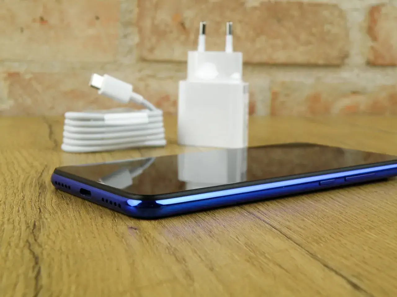 Niebieski Redmi 7 Pro leży obok białej ładowarki i kabla USB na drewnianym blacie.